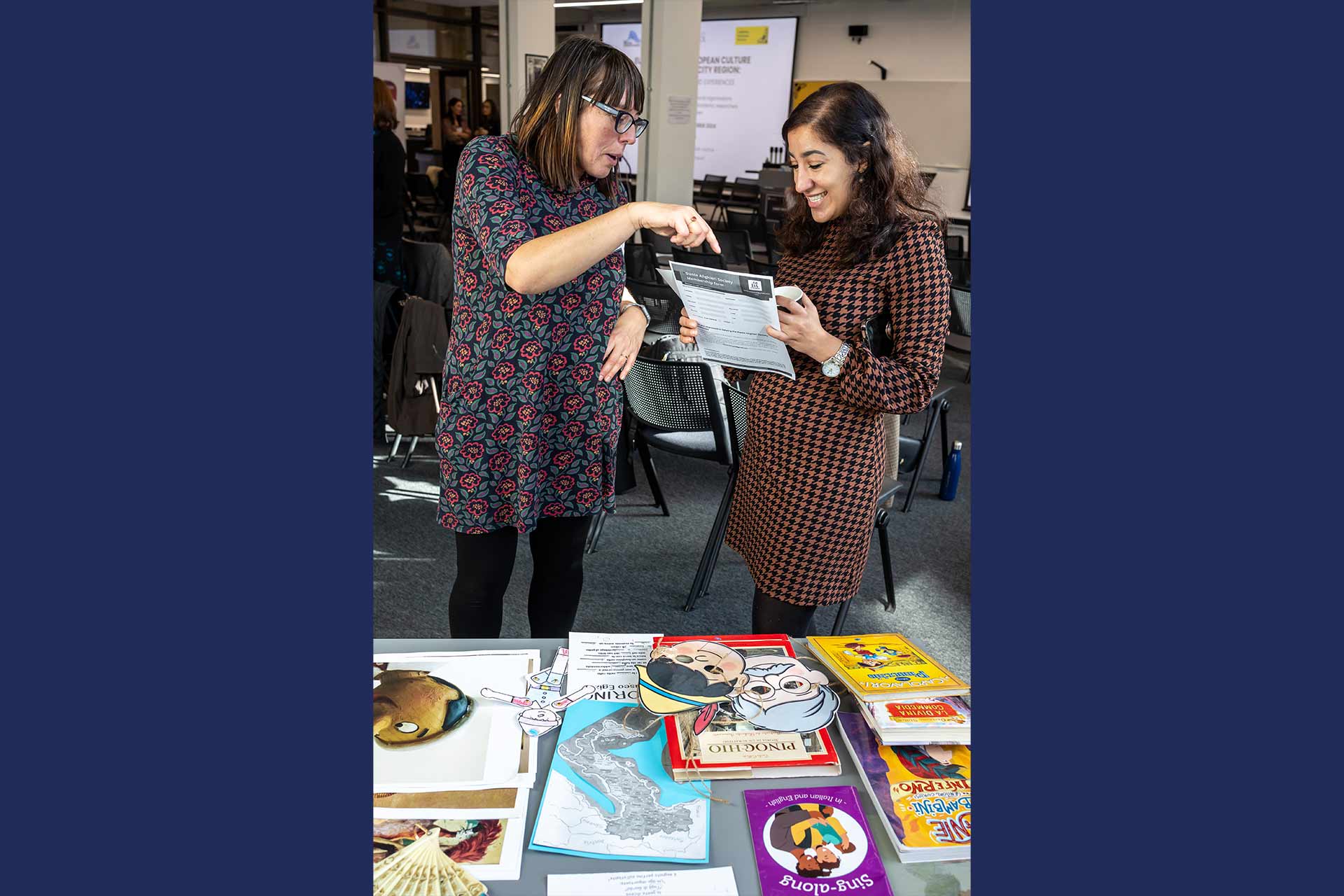 Two people holding and looking at event literature in front of a table with foreign language books.