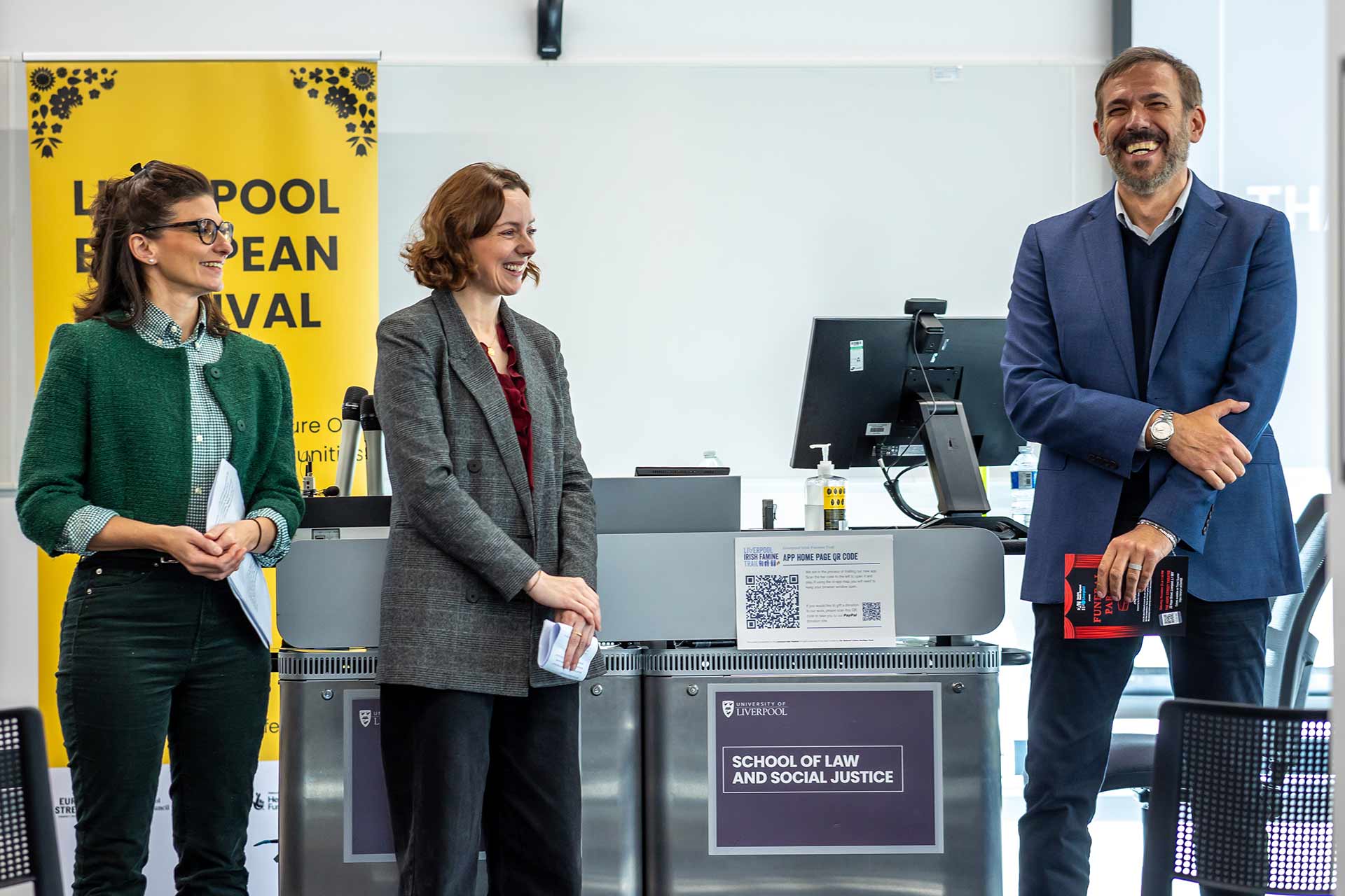 Three people standing and smiling in front of a presentation screen at an event.