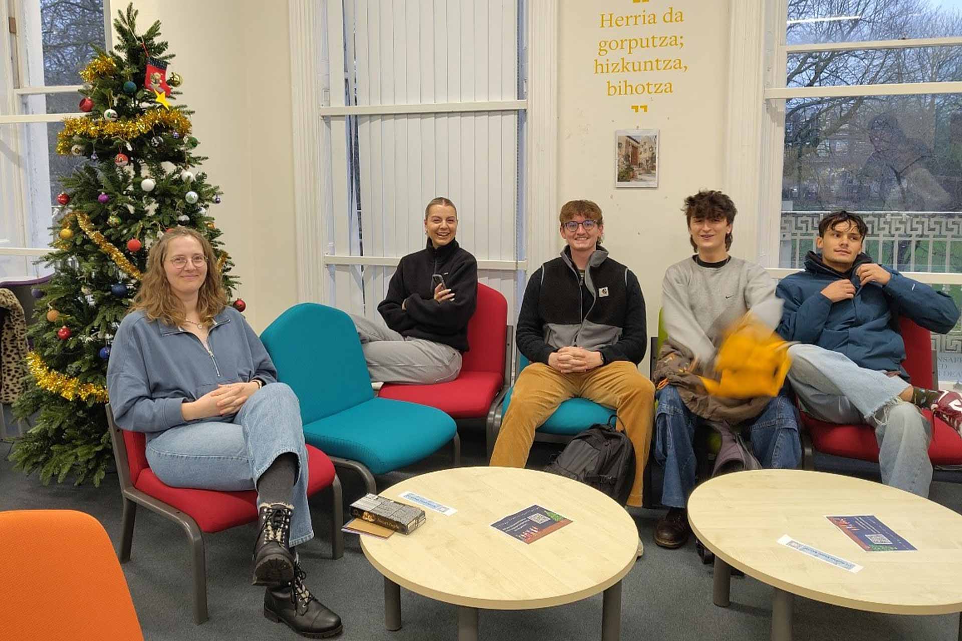 Four people sitting around on low chairs in the Language Lounge with a Christmas tree in the background.