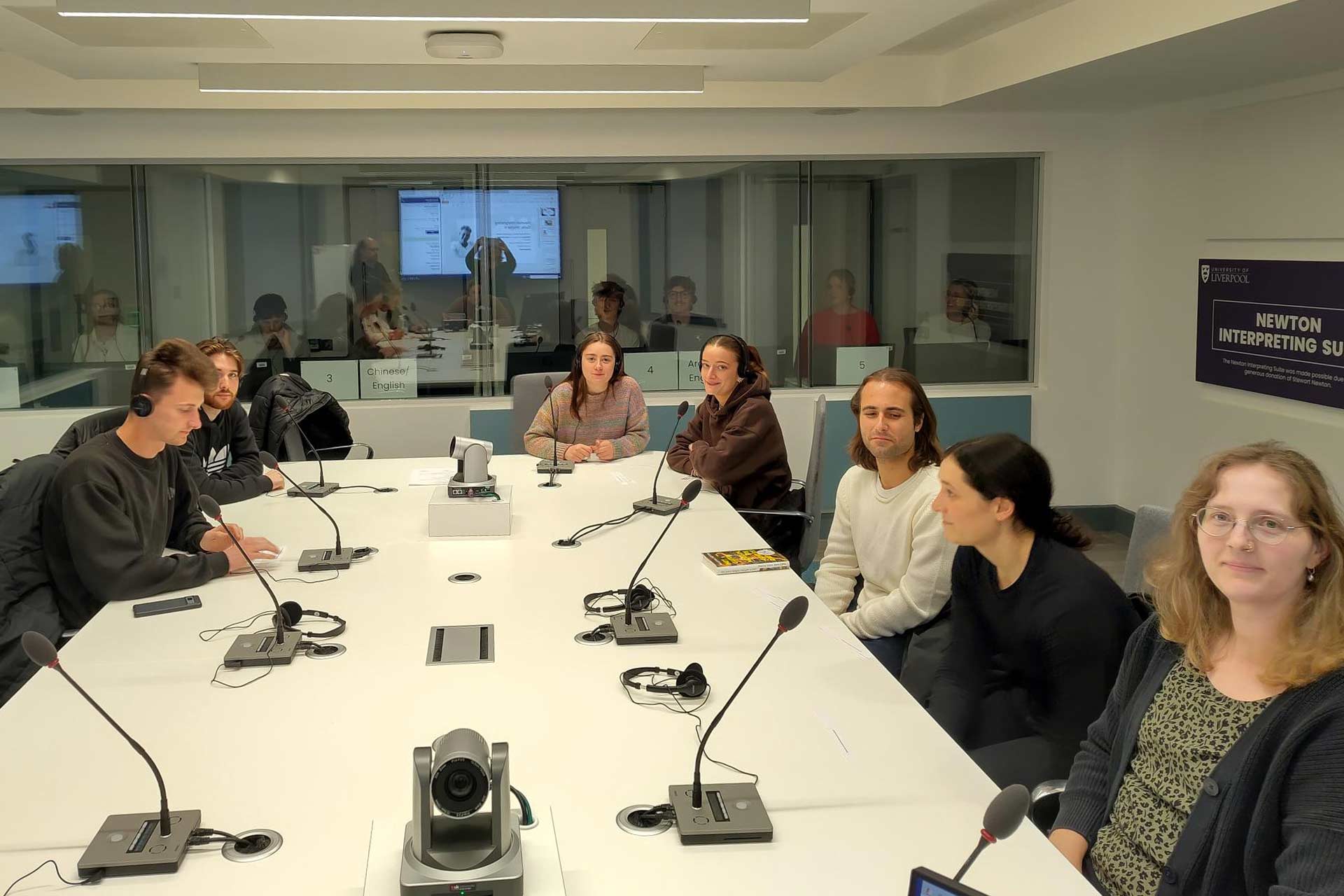 A group of people including students and teachers sitting around a table with microphones and headphones