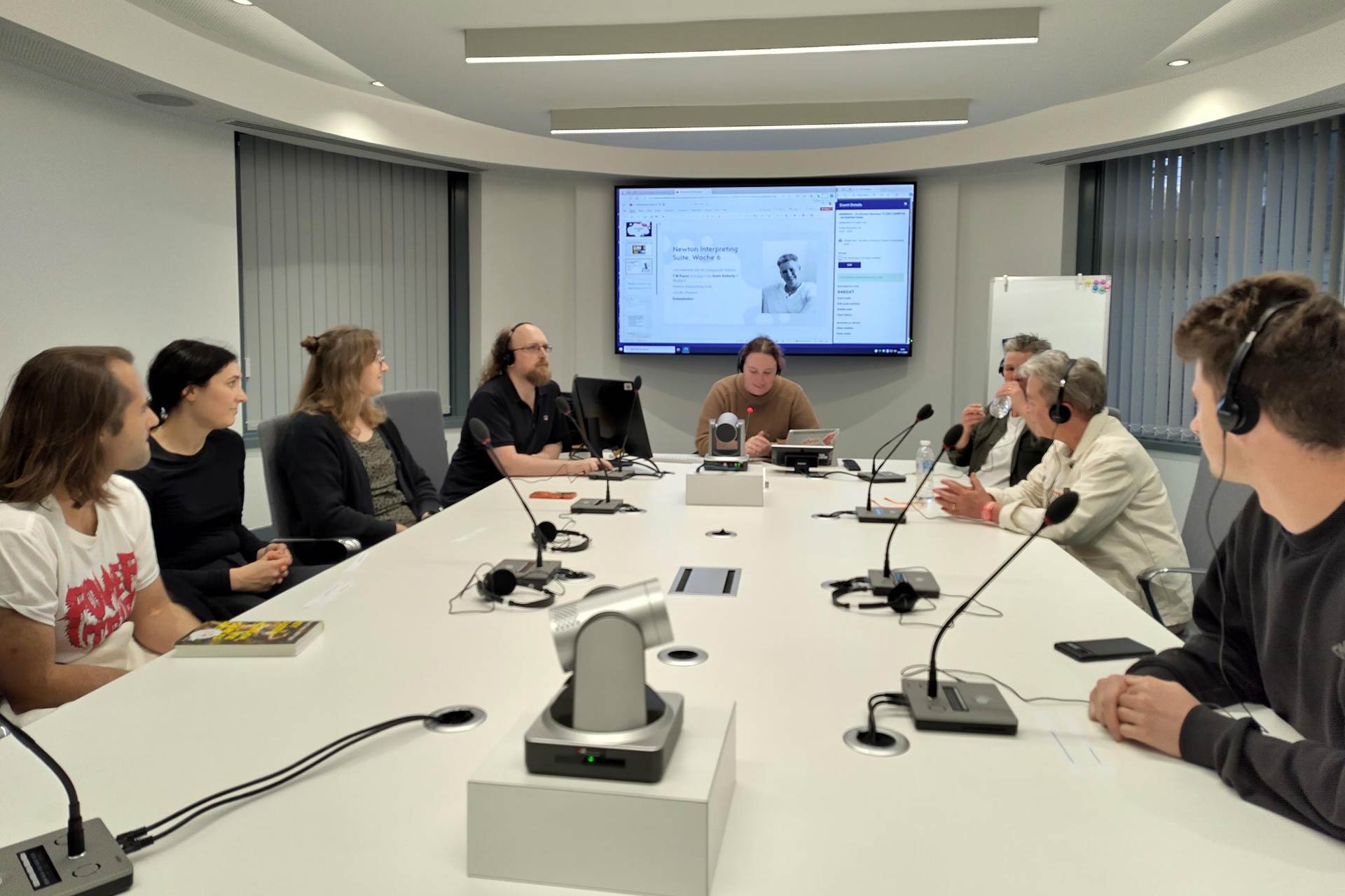 A group of people including students and teachers sitting around a table with microphones and headphones