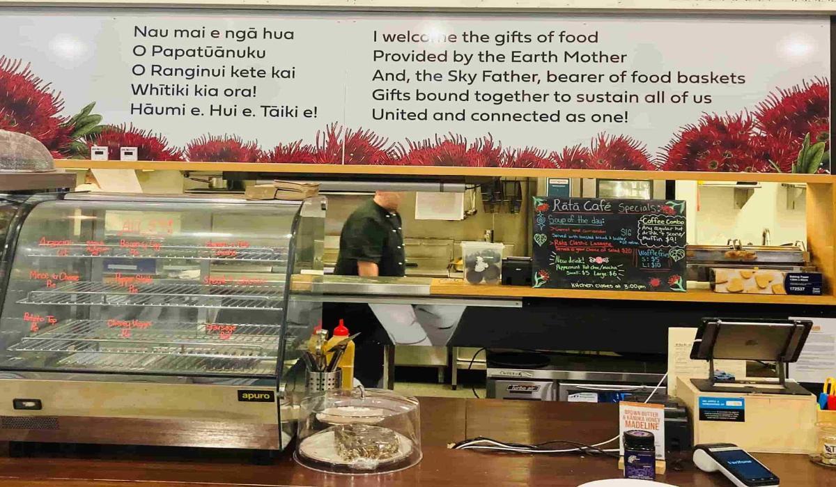 A cafe counter with a signboard behind with Maori and English writing