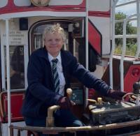 A woman, Wendy O'Neill, smiling on pretending to operate the controls on a tram