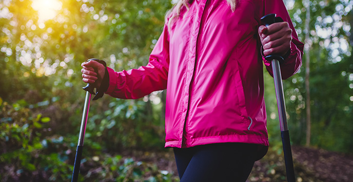 Close-up of a person with walking poles, walking through woodland.