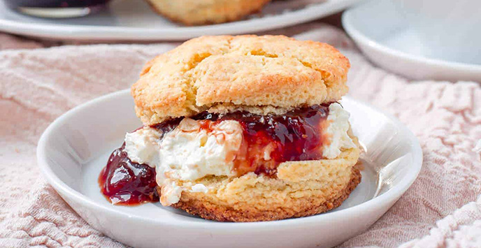 A scone with jam and clotted cream on a small plate.