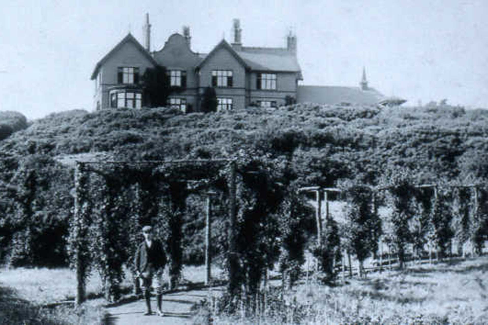 A black and white photo of a person standing on a path in the grounds of Ness.