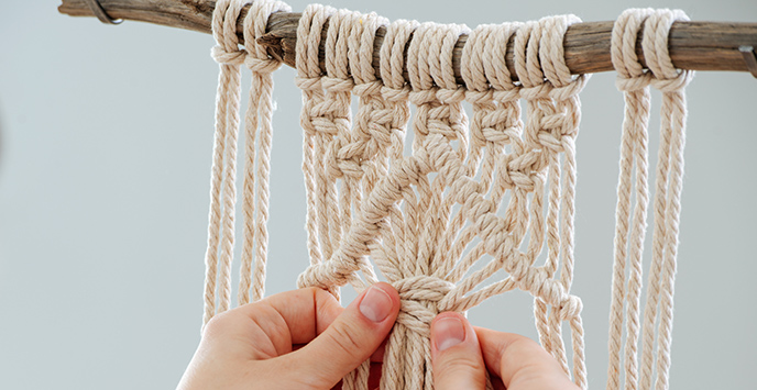 A person works on a macrame piece, weaving ropes and making knots.