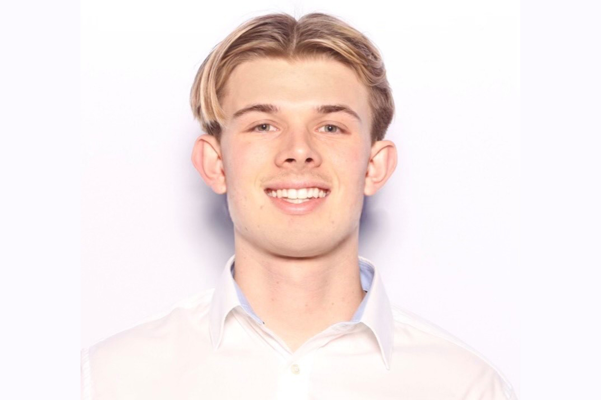 A headshot of a young man with light coloured hair wearing a white shirt smiling