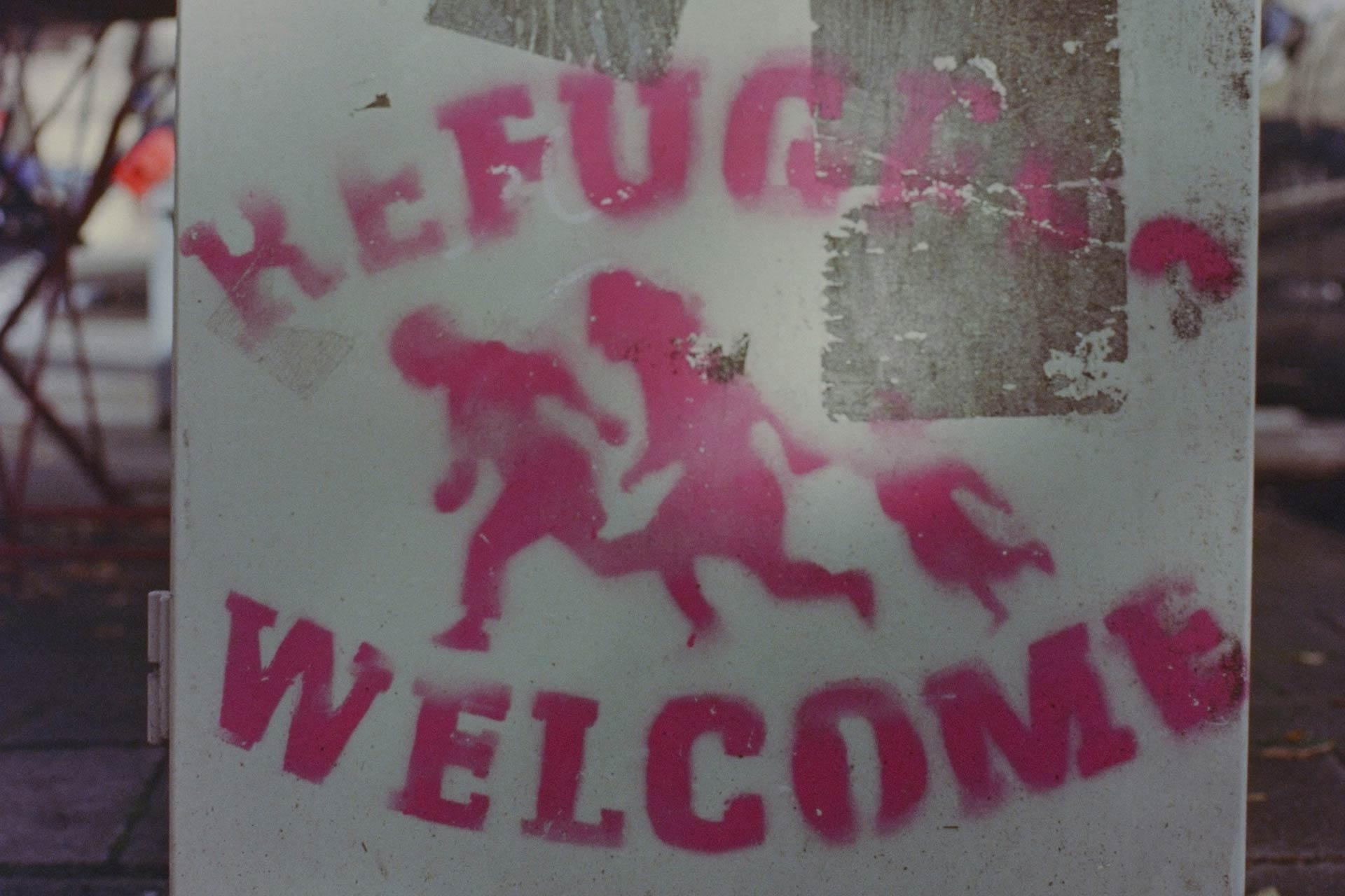 Stencil on wall that reads 'refugees welcome'