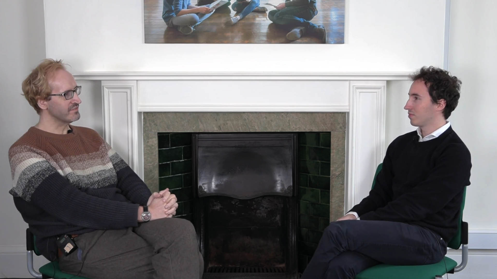 Two men sitting opposite each other, on the left an older man with glasses and lighter coloured hair is Andrew Roe-Crines and on the right is a younger brown haired man.