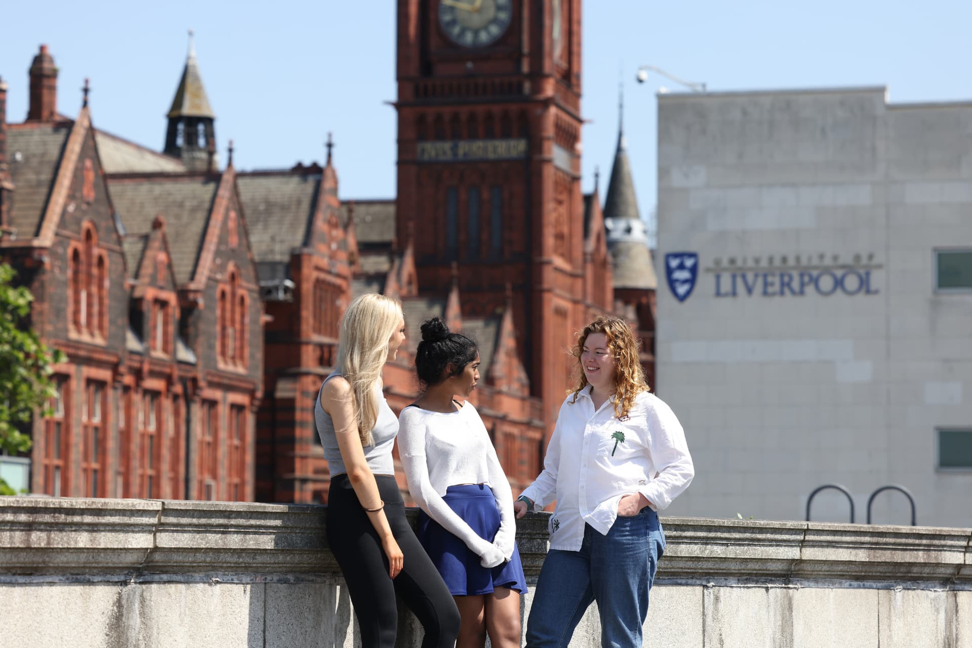 Three students standing on a rooftop on campus with the Victoria Gallery and Museum behind them.