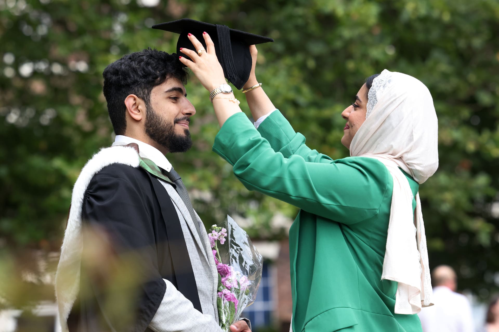 A woman placing a graduate cap on a student's head.