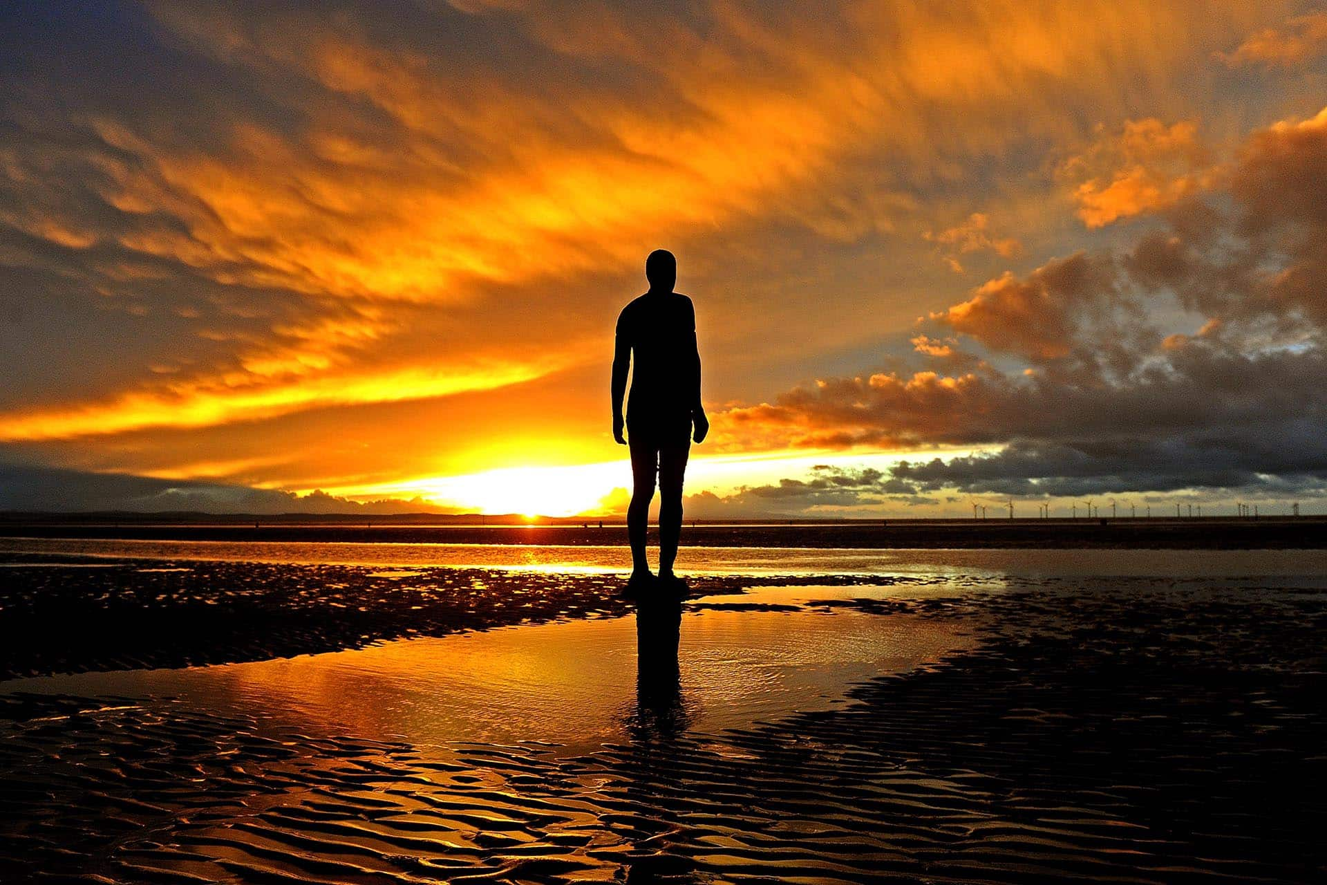 Anthony Gormley iron man statue against a dramatic sunset