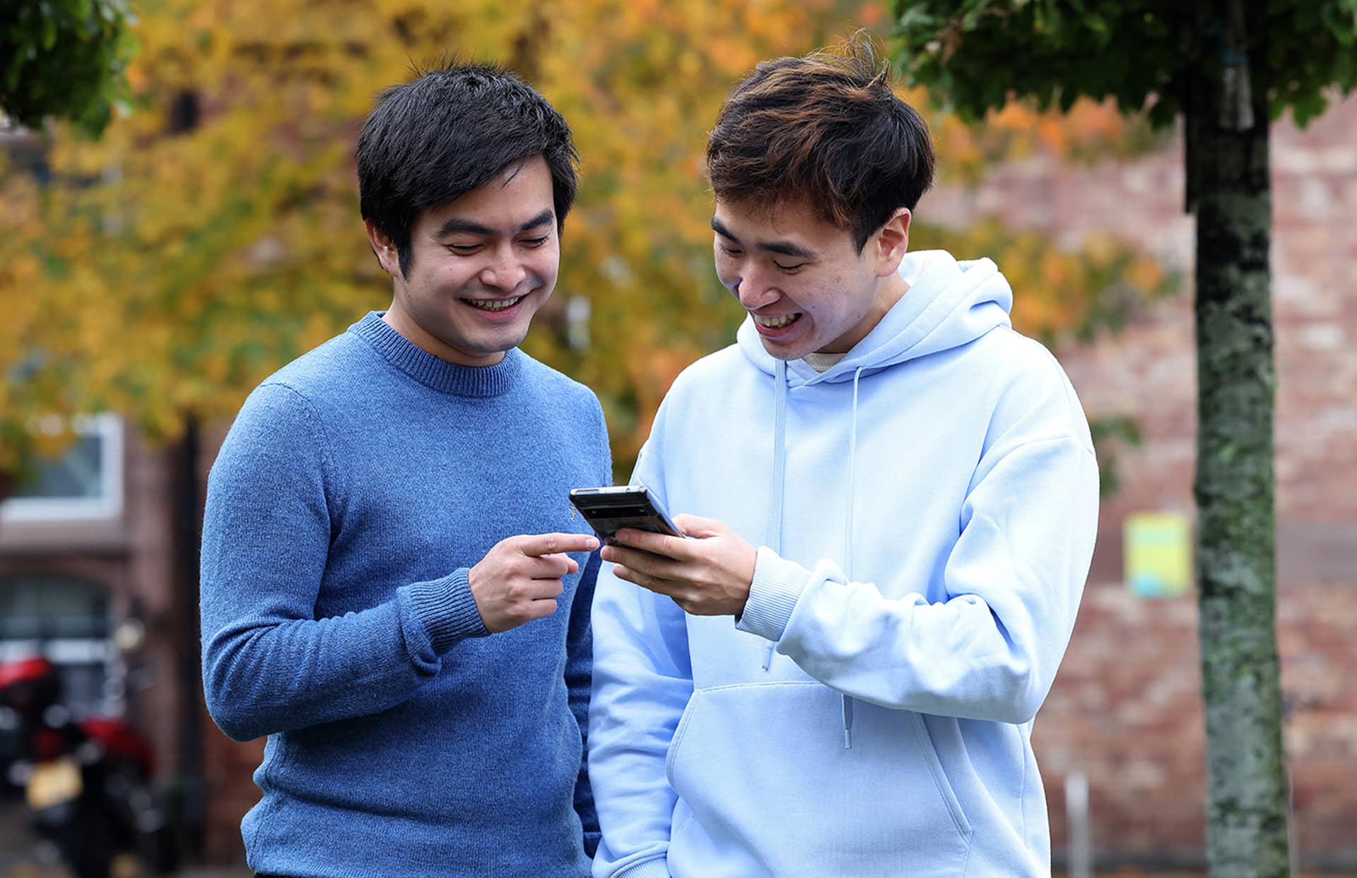 Two students walking through campus chatting looking at a phone