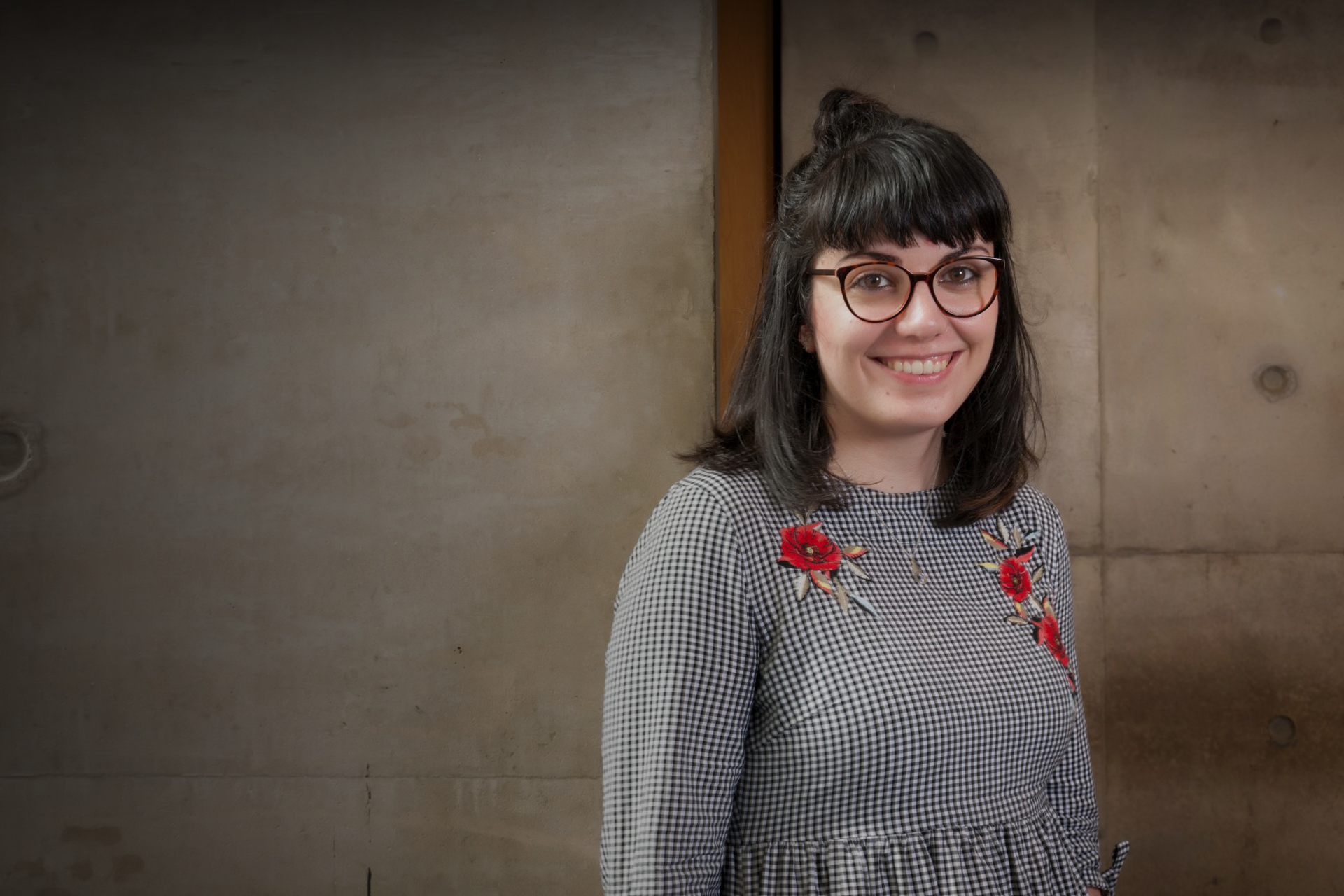 A postgraduate student smiling in front of a concrete wall.