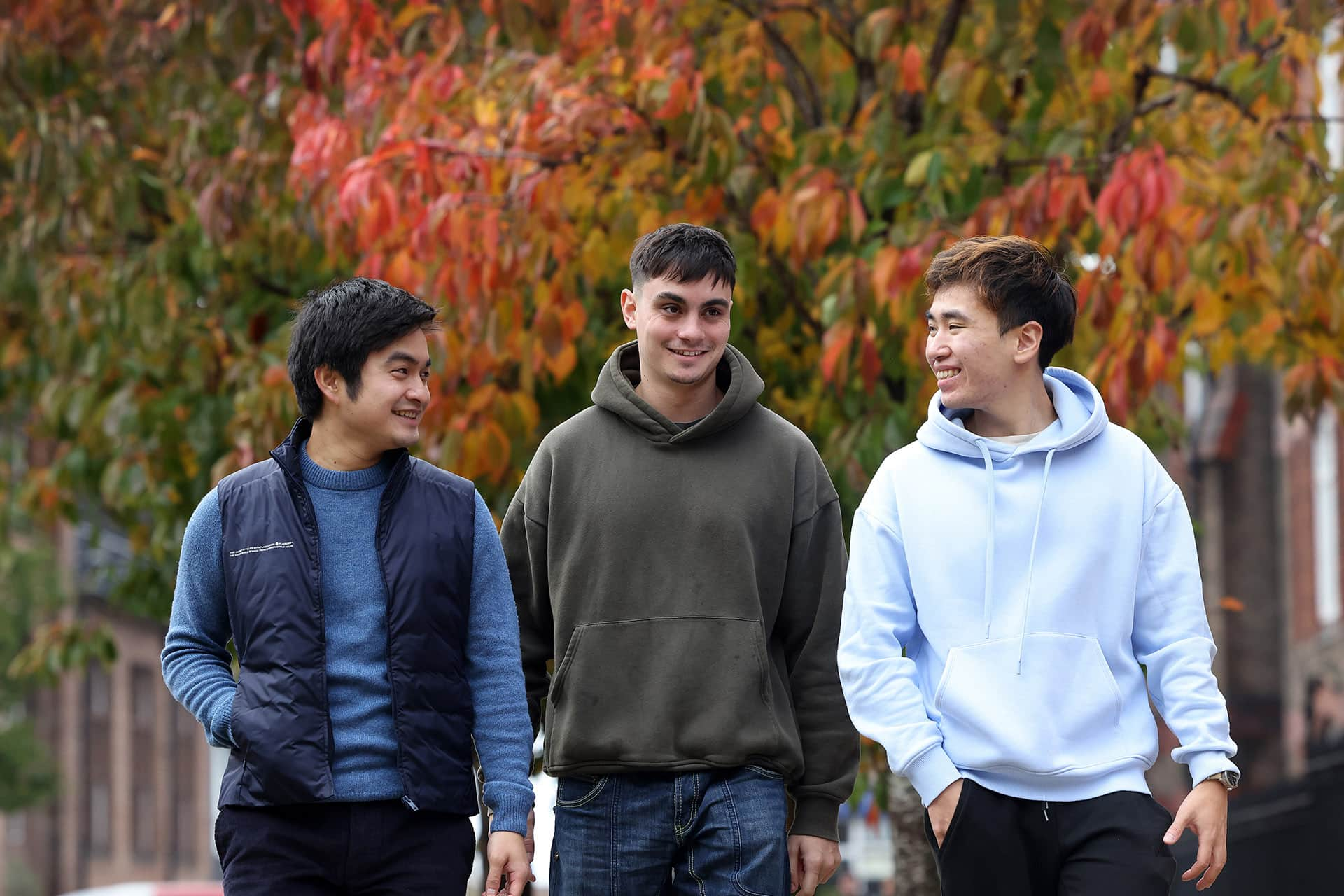 Group of male students walking through campus with autumn trees in the background