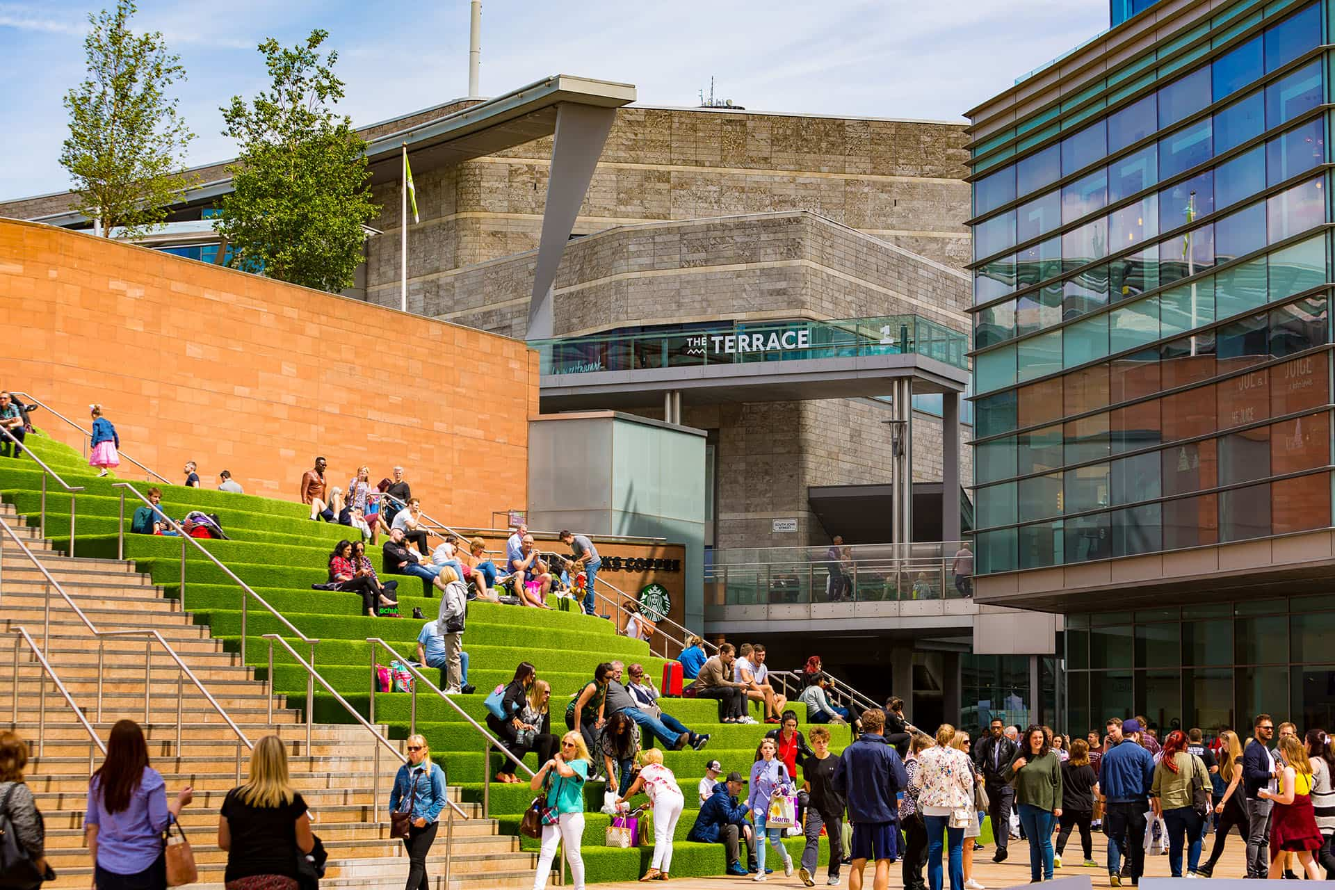 Liverpool One shopping area with people sitting on the steps in the sunshine