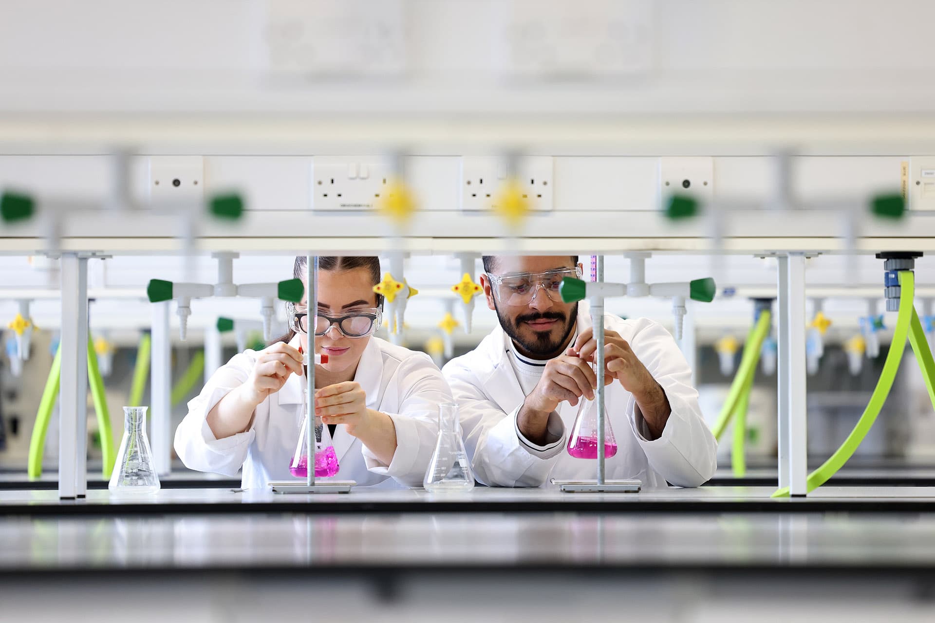 Two people working together in a lab filling beakers with solution