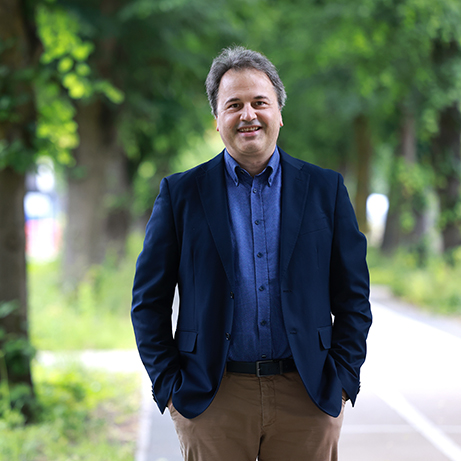 A photograph of Professor Graziano Venanzoni smiling in front of a background filled with trees and sunlight