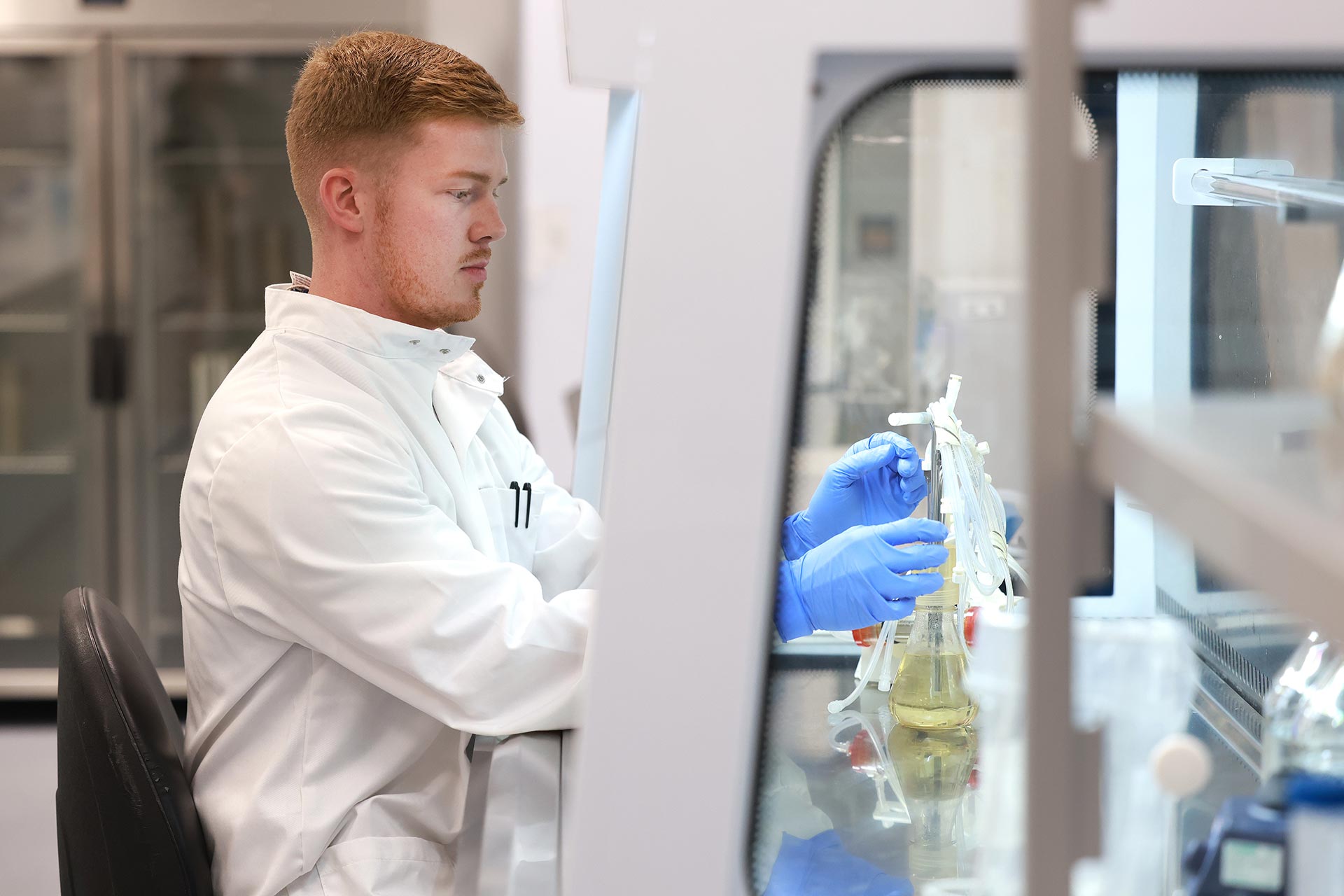 Researcher wearing a white coat and gloves holding up a lab sample