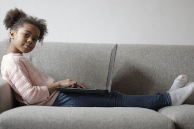 A young girl sitting on a couch with a laptop