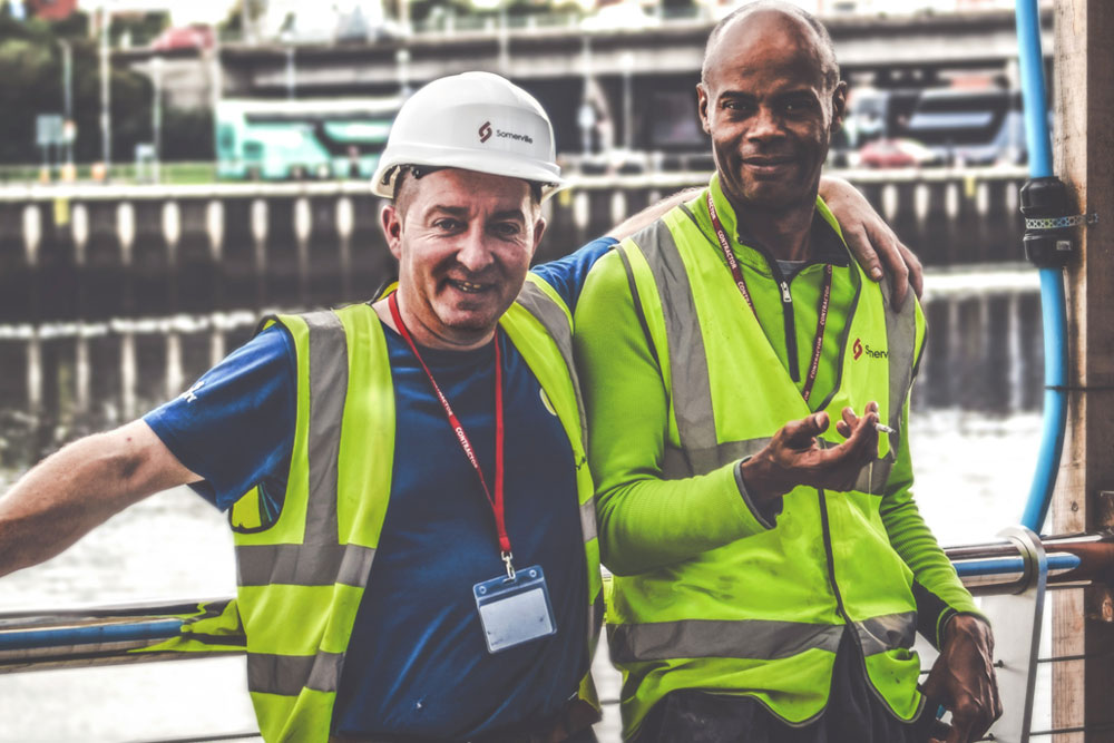 Two workmen standing against a railing