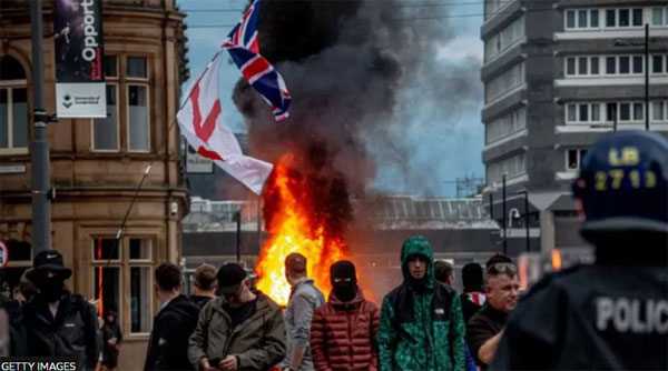 A crowd of rioters with flags and flames. Image: BBC and Getty Images