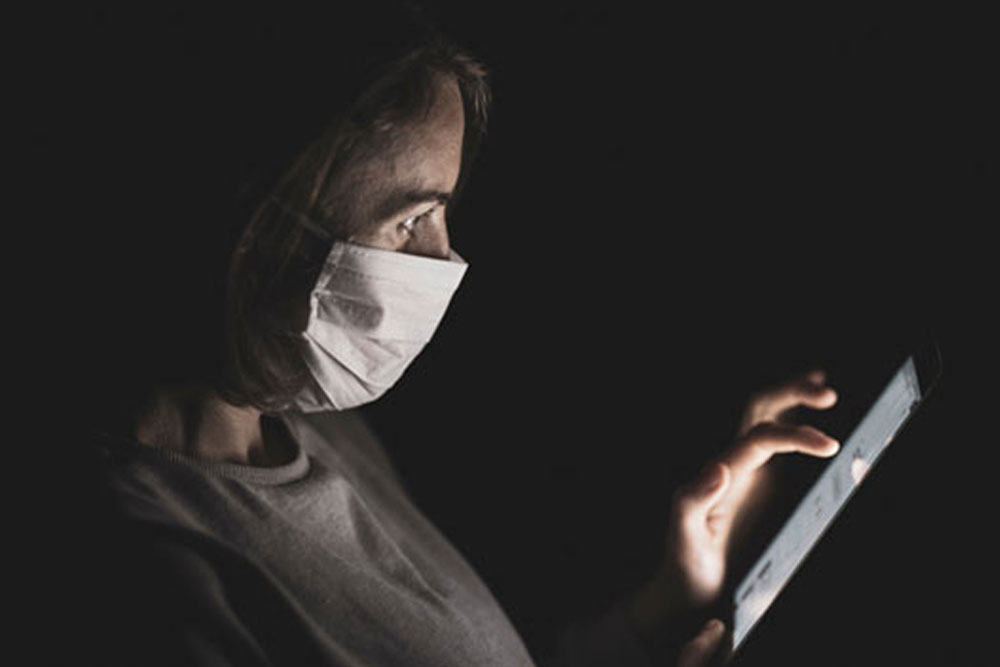 A woman wearing a face mask looking at a tablet