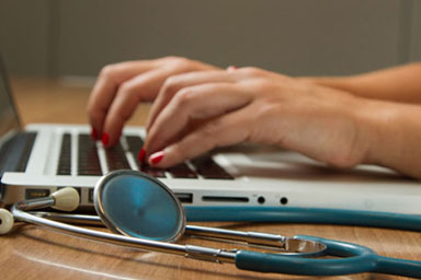 Hands typing on a laptop near a stethoscope