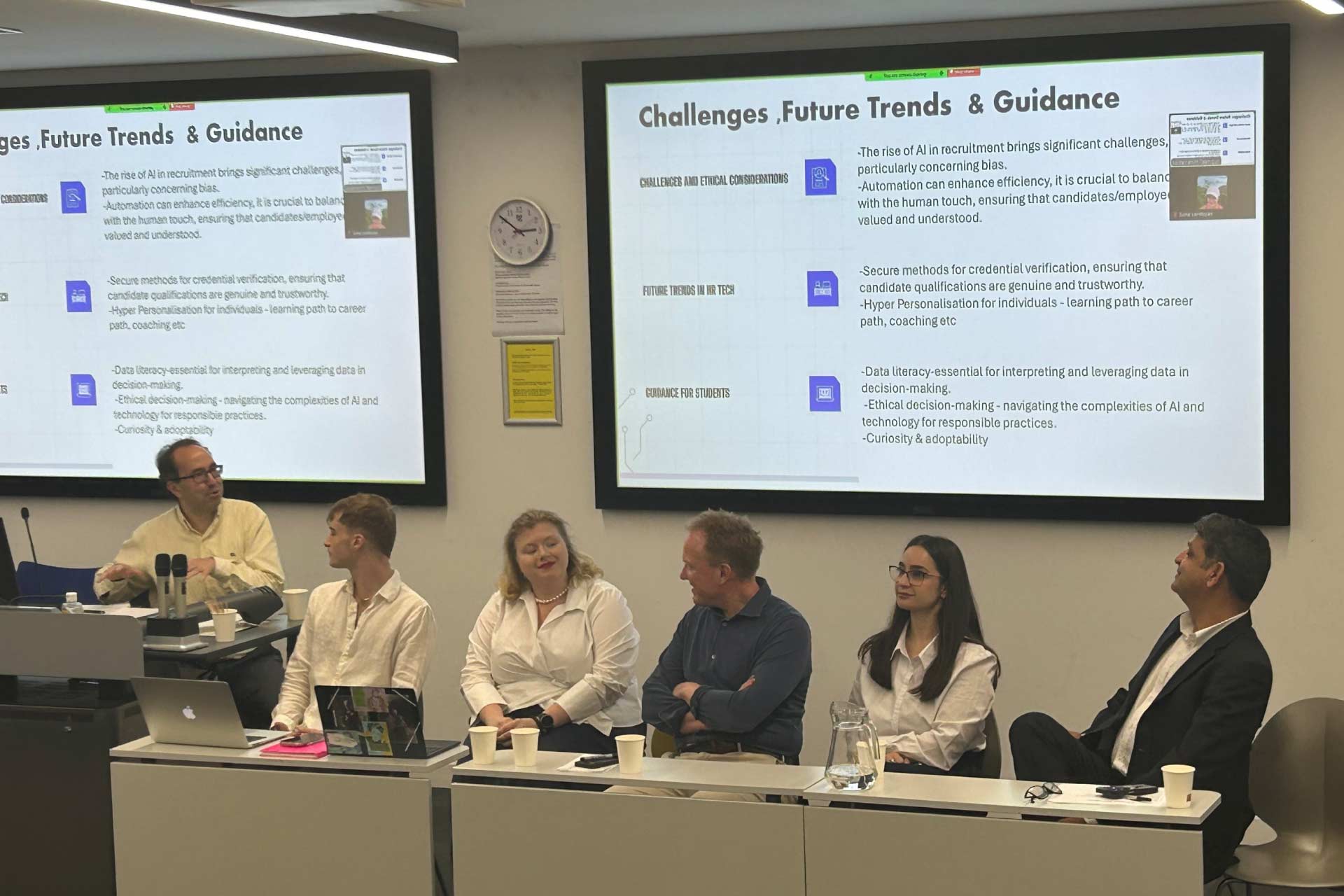 Host, three speakers and two MSc students sitting at a long table facing the lecture theatre audience