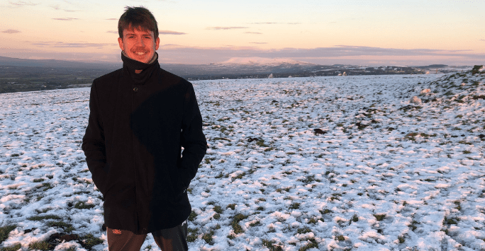 student standing in the snow with a colourful sky background