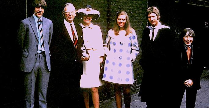 a graduate in graduation gown poses with family members