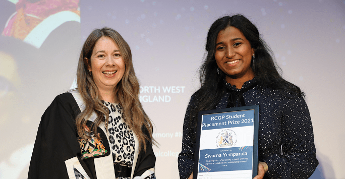 woman wearing robe presents certificate to woman in formal wear