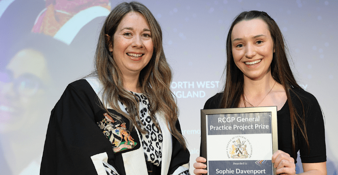 woman wearing robe presents certificate to woman in formal wear