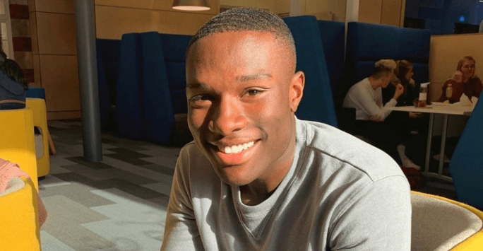 man smiles to the camera indoors in a ray of sunshine