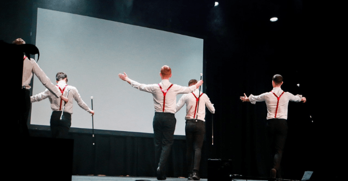 performers wearing shit shirts, red braces and black trousers on stage