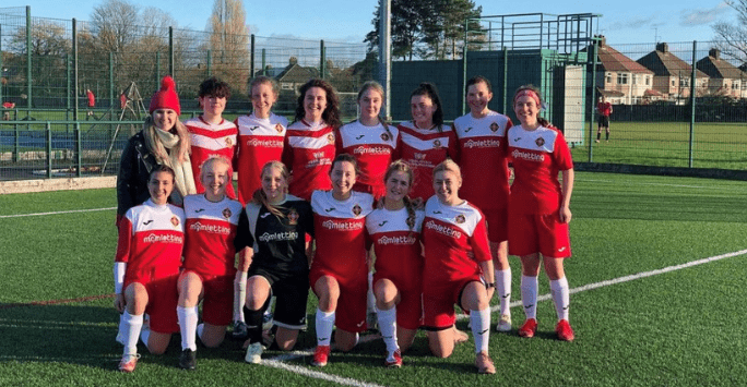 women's football team pose for group shot on football pitch