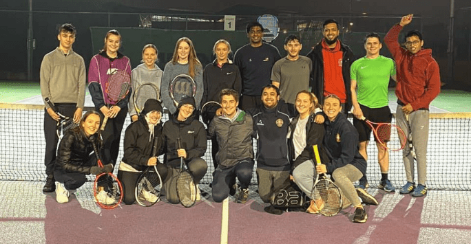 group of people pose with rackets on tennis court