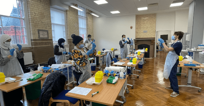 People wearing PPE practice clinical skills in a classroom setting