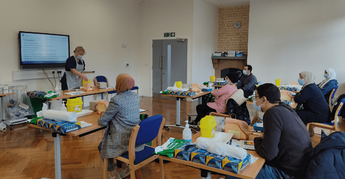 People wearing PPE practice clinical skills in a classroom setting