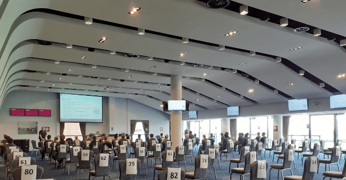 students take part in a briefing session in a large hall with numbered chairs