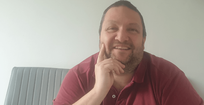 man wearing a red polo shirt smiles to camera