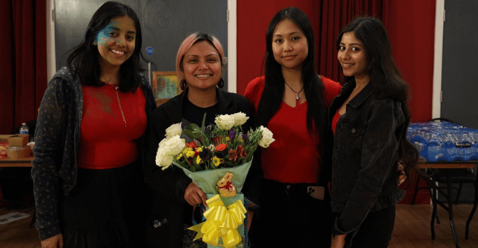 three women standing in a line, one of them holding a bouquet of flowers