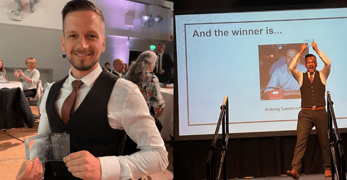 man in tie and waistcoat poses with award and accepts award on stage