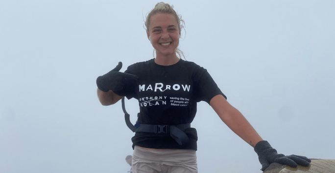 woman does a thumbs up at top of mountain