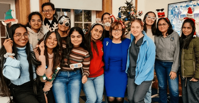 professor and students pose with festive props in front of a christmas tree