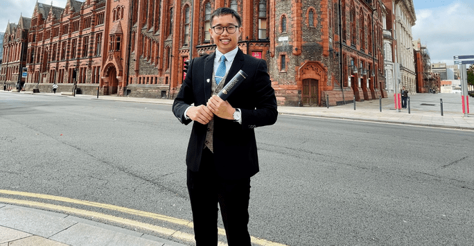 man in suit poses with degree scroll in front of VGM