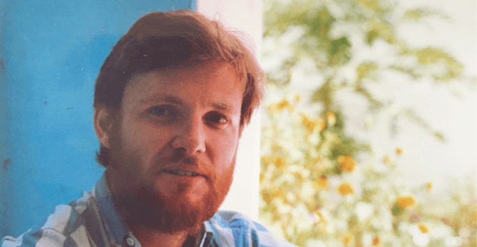 man wearing blue shirt sat at window with trees outside