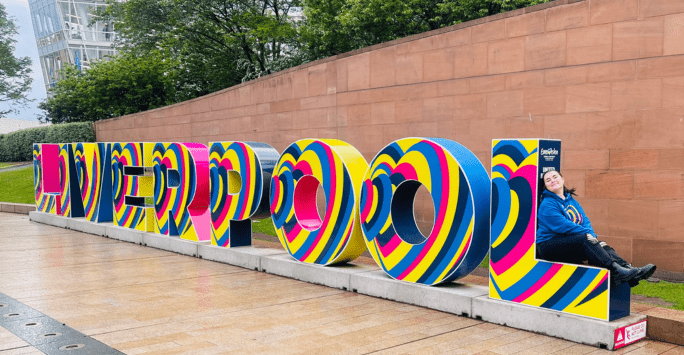 woman sits on Eurovision themed Liverpool sign