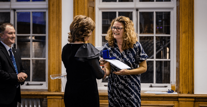 a woman presents a certificate and medal to a woman who is smiling